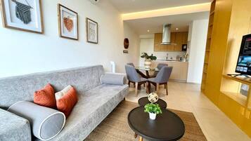 A modern living room with a grey sofa, a coffee table with a plant, and a dining area with chairs and a table.