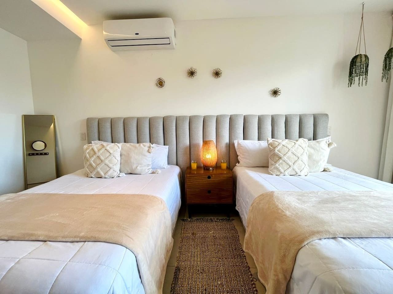 A hotel room with two beds, a nightstand with a lamp, and an air conditioning unit.