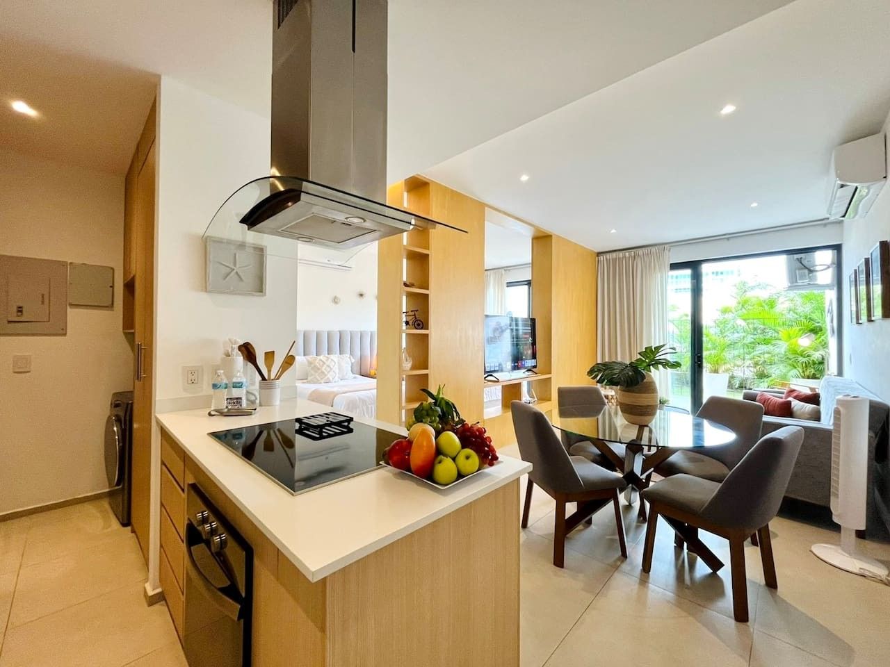 A modern kitchen with a central island, dining area with chairs, and a view of greenery outside.