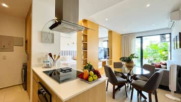 A modern kitchen with a central island, dining area with chairs, and a view of greenery outside.