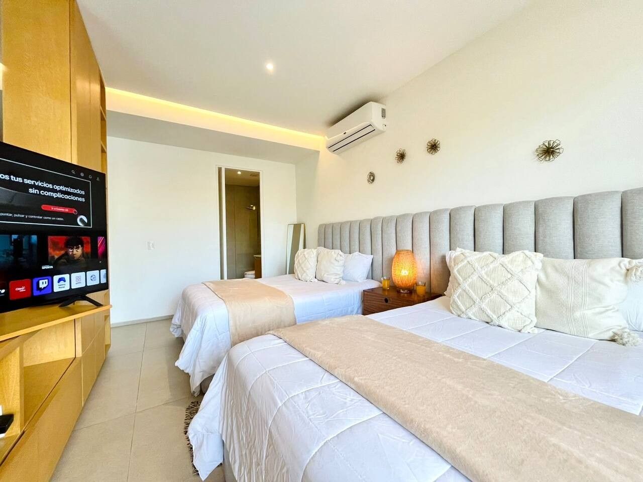 A hotel room with two beds, a television, and an air conditioning unit.