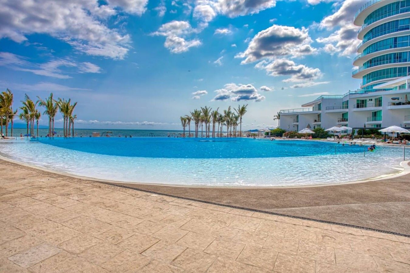 A large outdoor swimming pool with a clear blue sky and palm trees in the background.