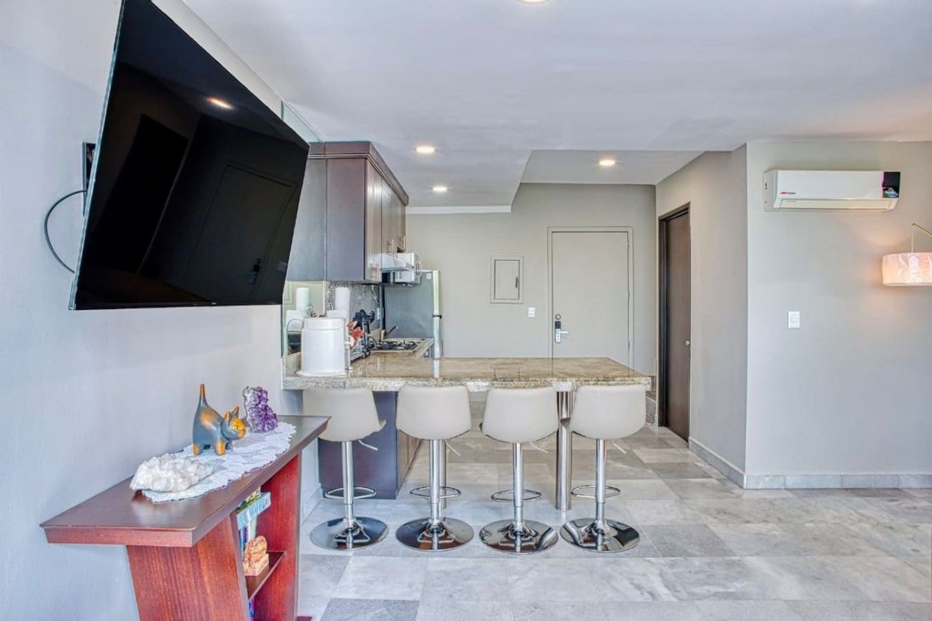 A modern kitchen with a built-in TV, bar stools, and a flat-screen TV mounted on the wall.