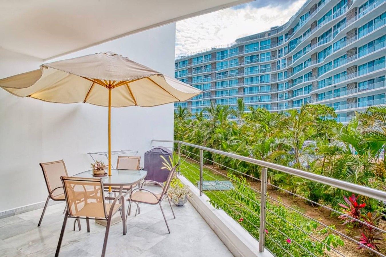 A balcony with a table and chairs, a large umbrella, and a view of a high-rise building with balconies.