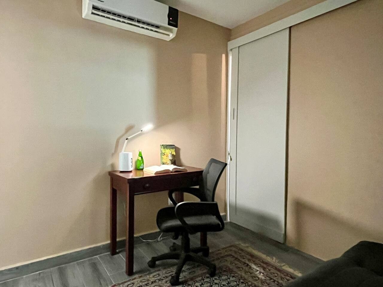 A small office space with a desk, chair, lamp, and an air conditioning unit.