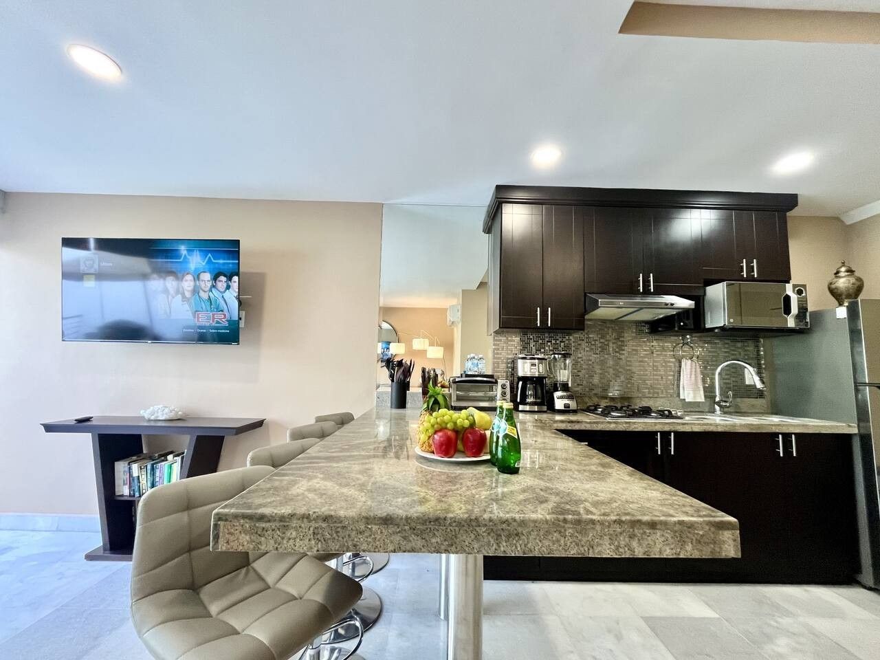 A modern kitchen with dark cabinets, a granite countertop, and a dining area with a cushioned chair.