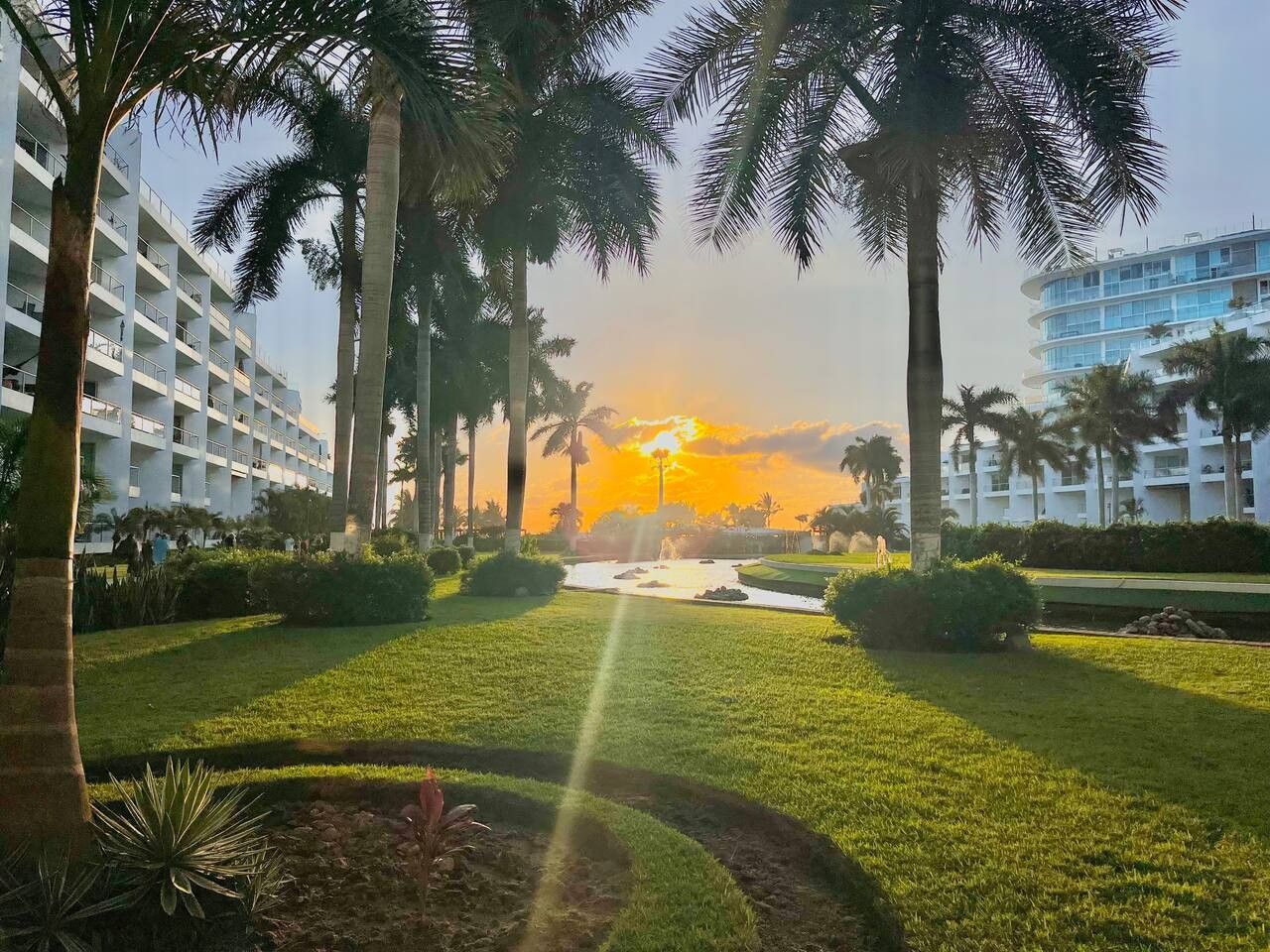 Een hotel binnenplaats met een zwembad, palmbomen en uitzicht op een zonsondergang.