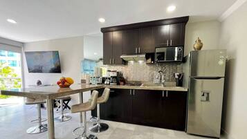 A modern kitchen with dark cabinetry, a stainless steel refrigerator, and a flat-screen TV mounted on the wall.