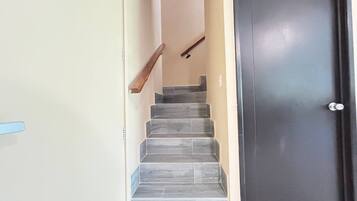 Escada que leva a uma porta escura, com uma parede clara de um lado e um corrimão de madeira.