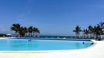 Ein klares, blaues Schwimmbecken mit Palmen und Liegestühlen, umgeben von einem weißen Sandstrand.