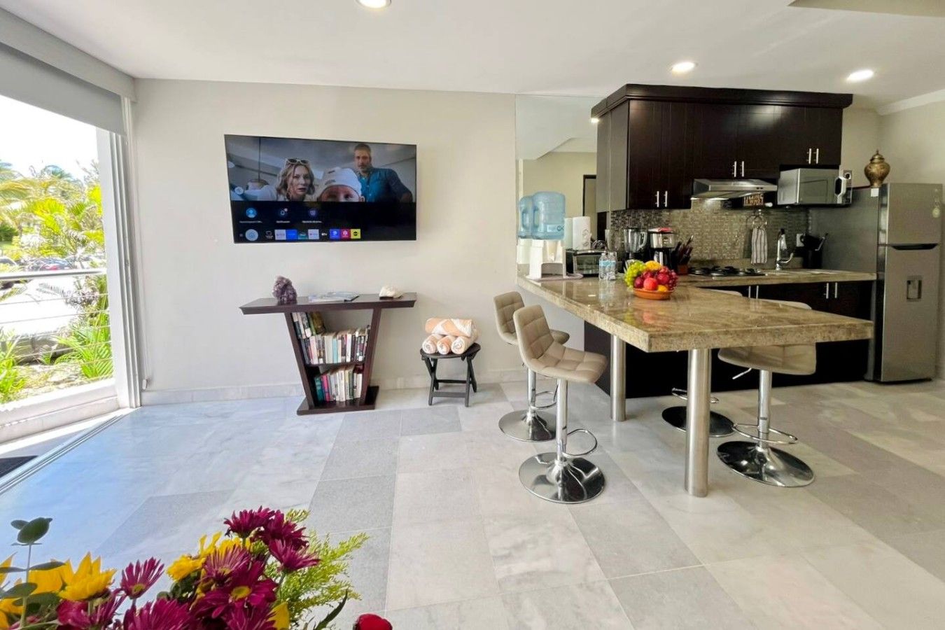 A modern kitchen with dark cabinetry, a large island, and a flat-screen TV mounted on the wall.