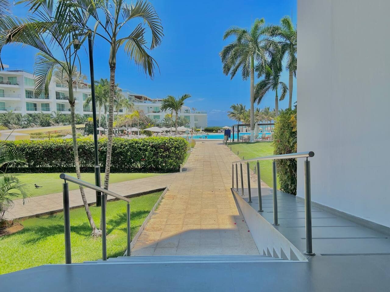 Ein Hotelkorridor mit Blick auf einen Pool, Palmen und einen klaren Himmel.