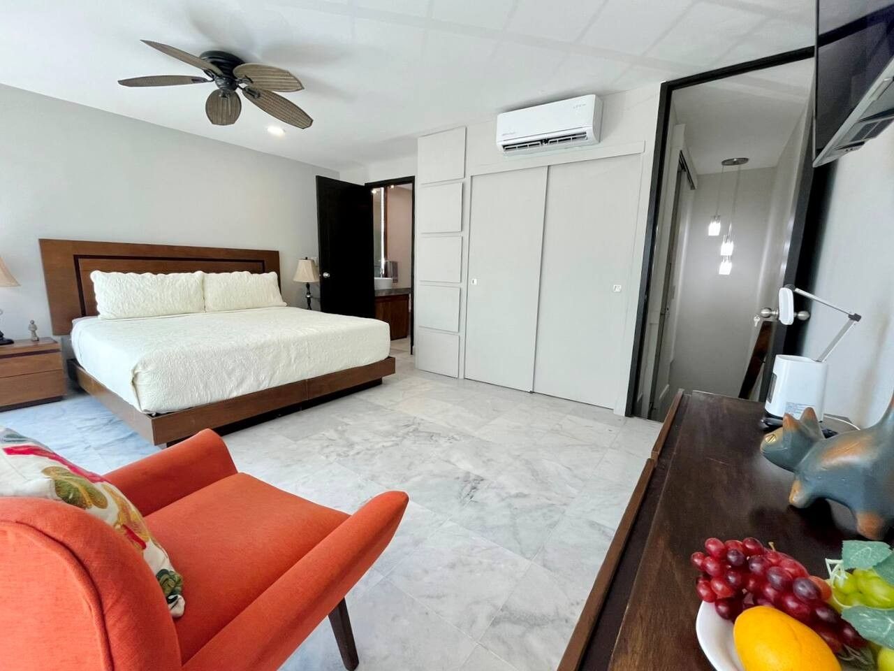 Quarto de hotel com cama, escrivaninha, cadeira, ar-condicionado e ventilador de teto.