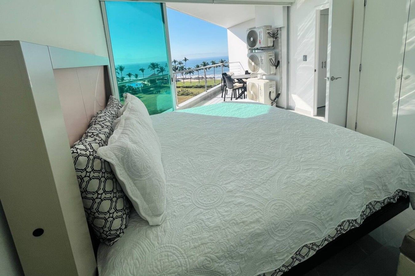 Une chambre avec un lit, une vue sur l’océan et un balcon équipé d’une table et de chaises.