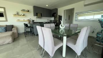 Una cocina moderna con armarios grises, una isla central y un comedor con mesa de vidrio y cuatro sillas.