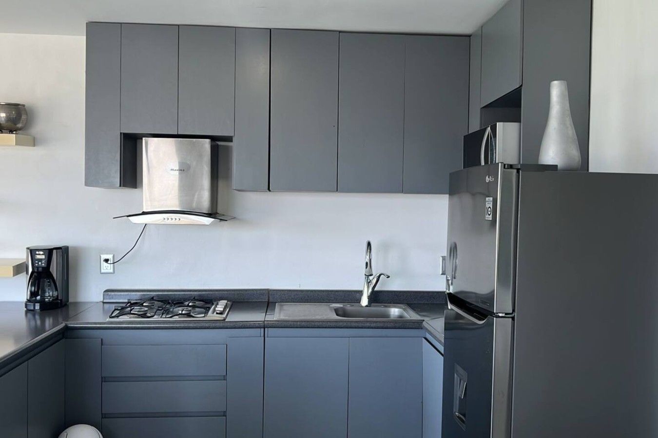 Eine moderne Küche mit grauen Schränken, einer Edelstahl-Dunstabzugshaube, einem eingebauten Gasherd, einer Spüle und einem Kühlschrank.