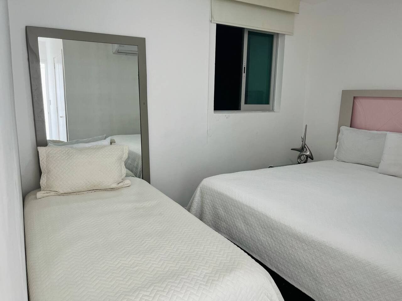 Une chambre d’hôtel avec deux lits, un grand miroir, une fenêtre et une sculpture métallique décorative.