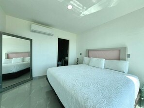 Habitación de hotel moderna con una cama grande, un espejo, un equipo de aire acondicionado y la puerta del baño.