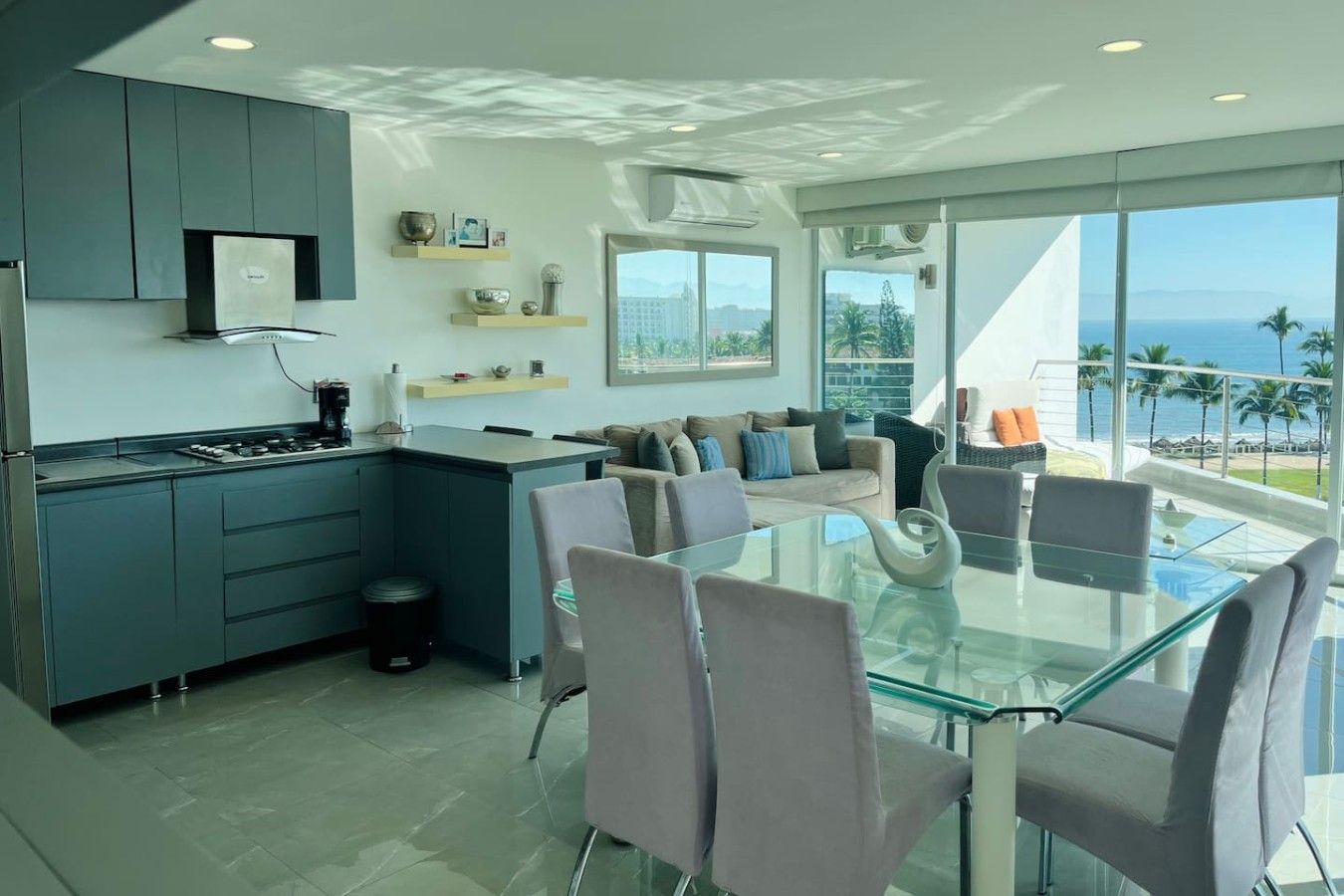 A modern kitchen with a dining area, large windows, and a view of the ocean.