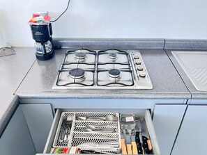 Una cocina con estufa a gas, cafetera y un cajón con utensilios.
