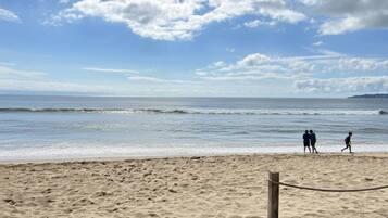 Une plage de sable avec un poteau en bois et une barrière faite de cordes, un ciel dégagé et une mer calme.