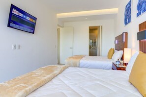 Una habitación de hotel con dos camas, un televisor instalado en la pared y una mesita de noche con una lámpara.
