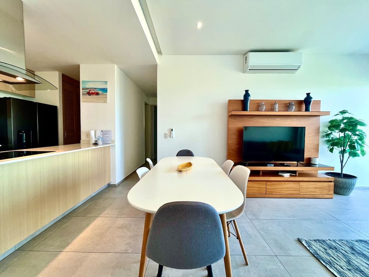 A modern kitchen with a dining area, a flat-screen TV, and a potted plant.
