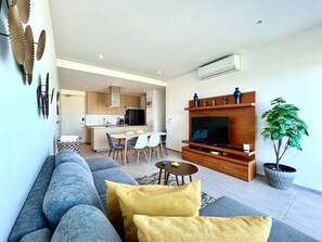 Una sala de estar moderna con un sofá, una mesa de centro y un televisor sobre un mueble de madera.
