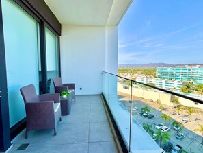 Un balcon avec deux fauteuils en osier et une petite table, donnant sur un parking et sur des bâtiments situés au loin.