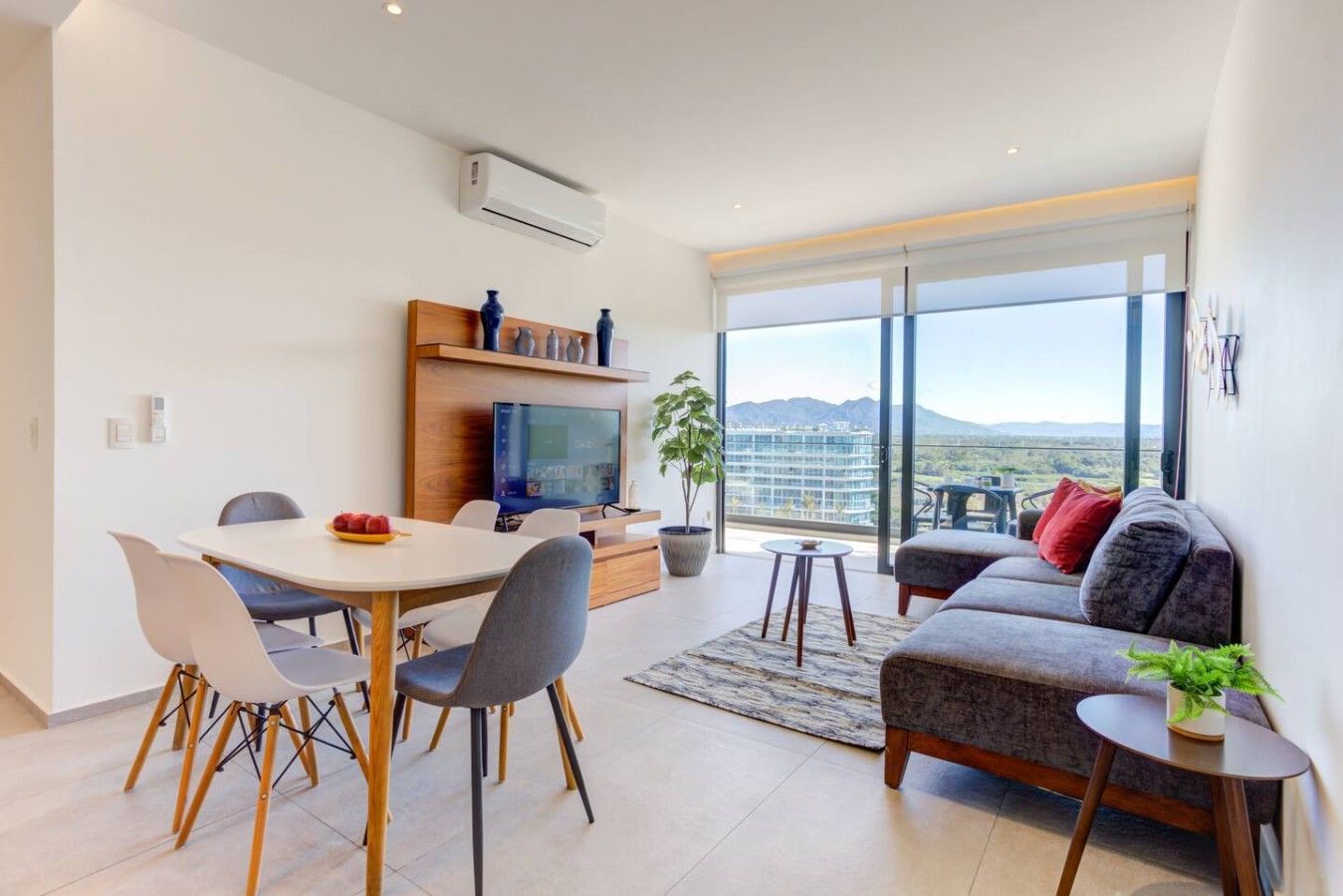 A modern living room with a dining area, a flat-screen TV, and a large window with a view of the city.