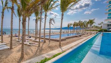 A pool area with a beach, palm trees, and a view of the ocean.