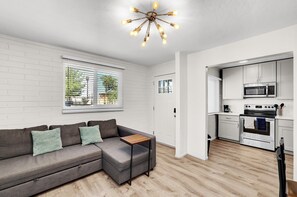 A modern living room with a grey sectional sofa, a small wooden coffee table, and a unique ceiling light fixture. - 2BR Walk to Main St · Free Parking · Pets OK (Gilbert)