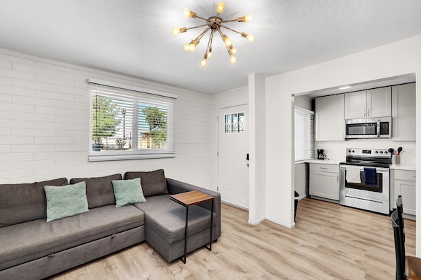 Een moderne woonkamer met een grijze hoekbank, een klein houten bijzettafeltje en een bijzondere hanglamp.