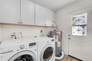 Un lavadero con dos lavadoras LG Direct Drive blancas, un calentador de agua y una puerta blanca con ventanal.