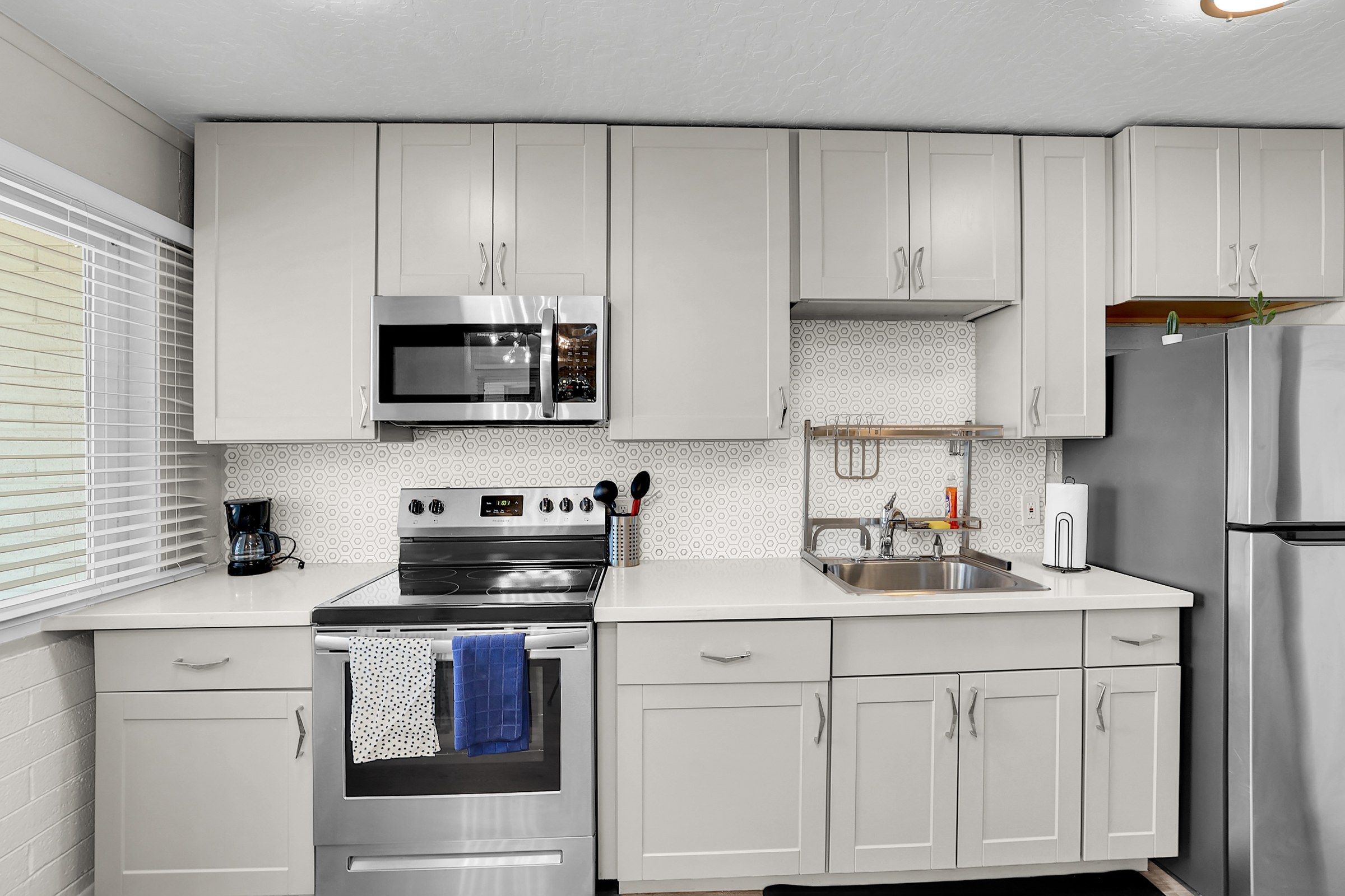 Una cocina moderna con armarios blancos, electrodomésticos de acero inoxidable y un ventanal con persianas.