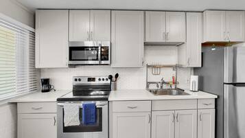 Una cocina moderna con armarios blancos, electrodomésticos de acero inoxidable y un ventanal con persianas.