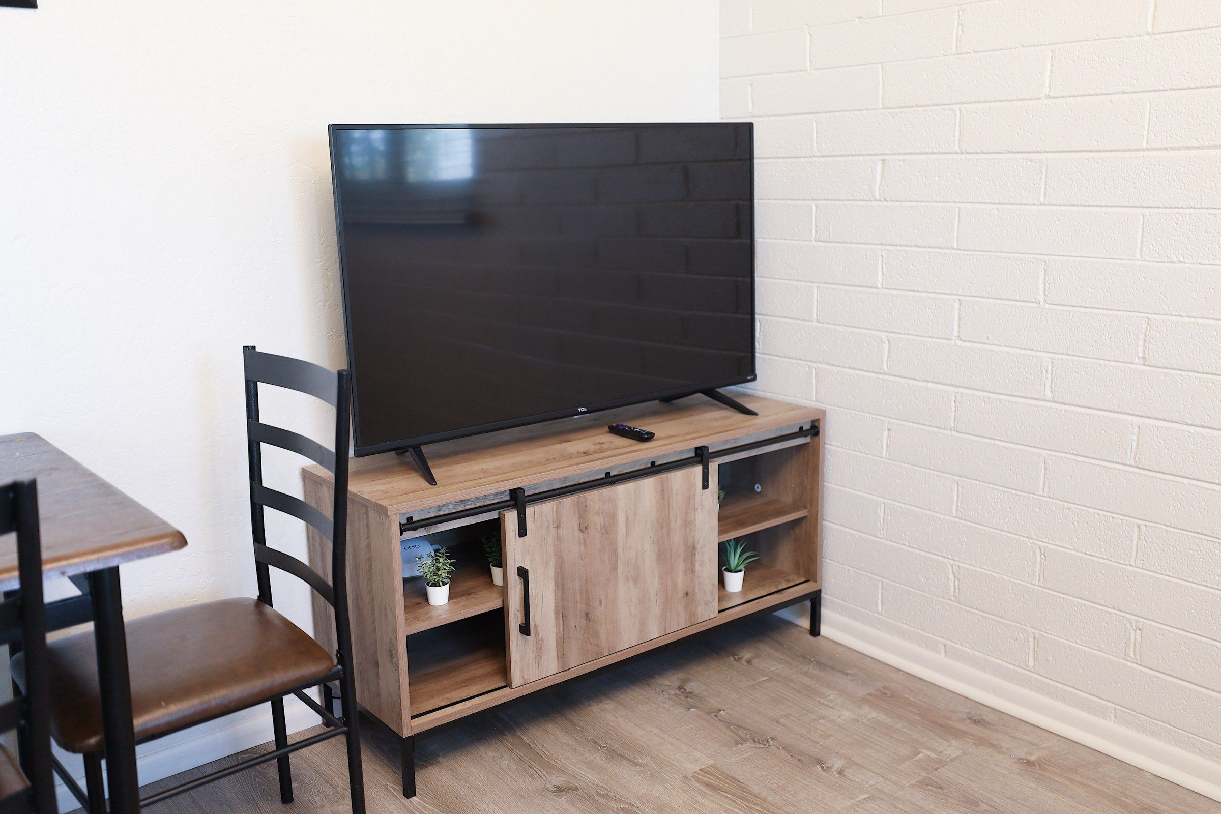 A TV on a wooden stand with a chair and a small table.
