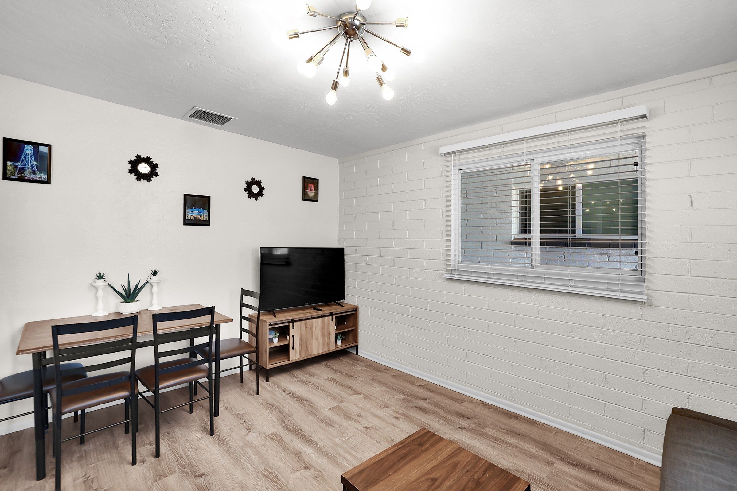 A modern living room with a TV, wooden furniture, and a white brick wall.