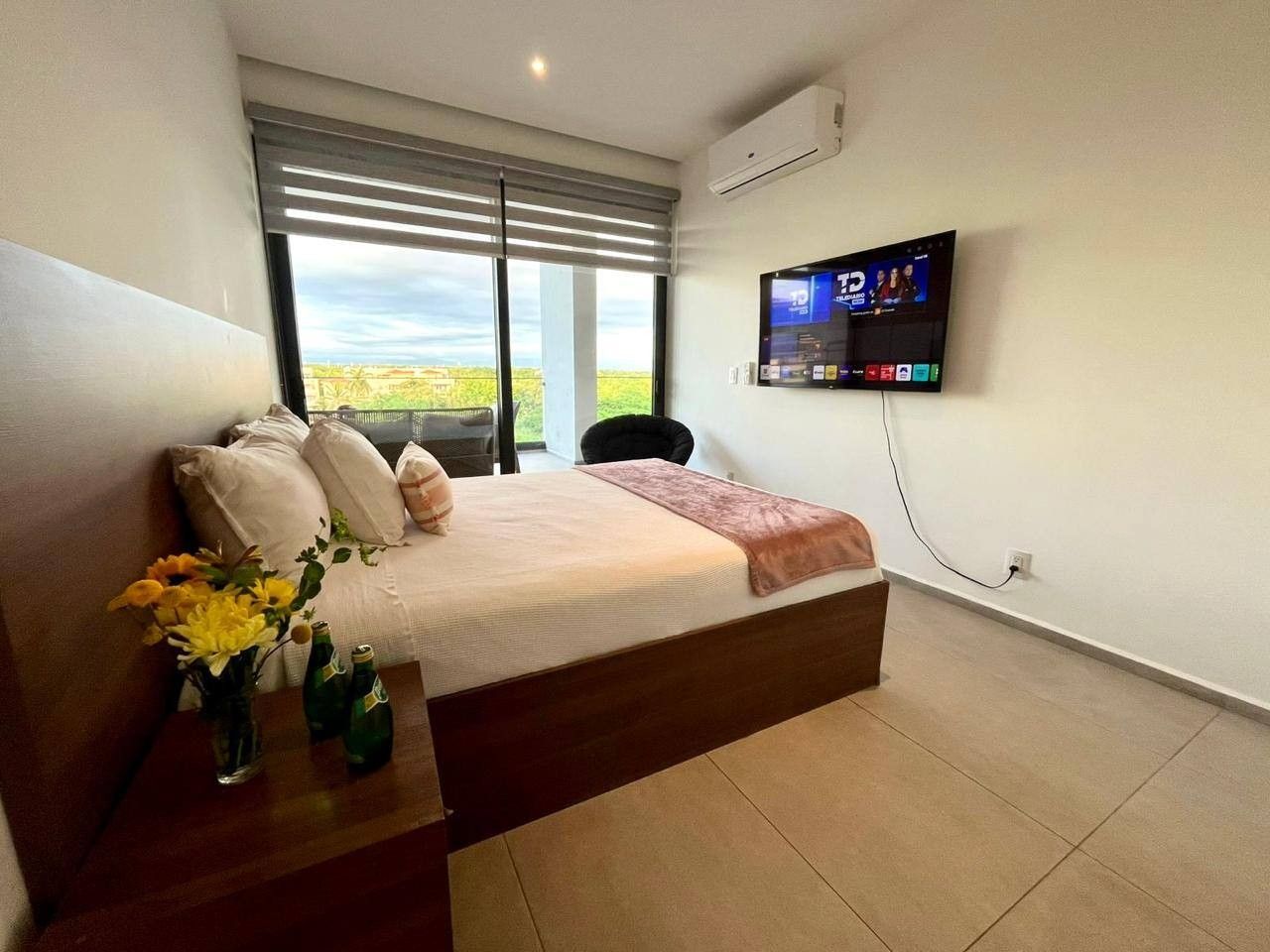 Quarto com cama, televisão na parede e janela com persianas.
