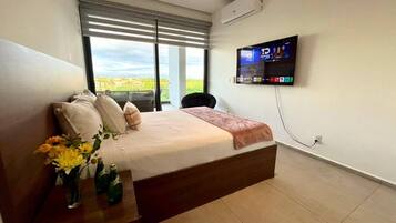Quarto com cama, televisão na parede e janela com persianas.