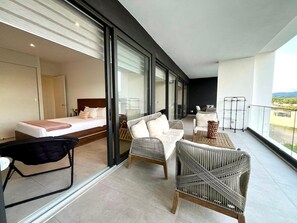 Una habitación de hotel moderna con balcón, una cama y dos sillones de mimbre.