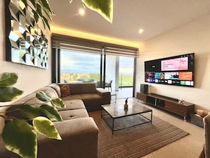 Uma sala de estar moderna com uma grande televisão de tela plana, um sofá, uma mesa de centro e uma janela ampla com vista.