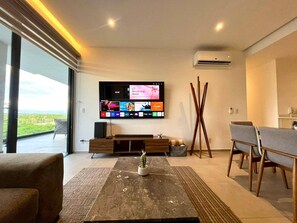 Una sala de estar moderna con un televisor de pantalla plana, un cactus como elemento central y un comedor con sillas y una mesa.