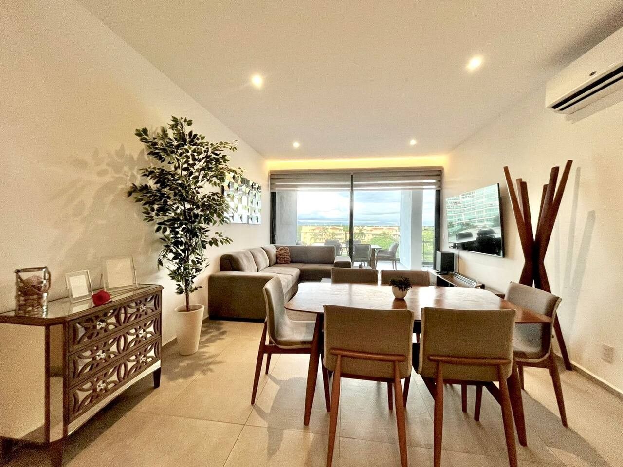 A modern living room with a sofa, dining table, chairs, a potted plant, and a TV.