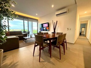 Una sala de estar moderna con comedor, un televisor de pantalla plana en la pared y un amplio ventanal con vistas al exterior.