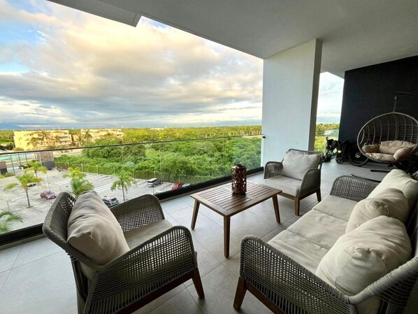 Un balcón con mobiliario de mimbre, una mesa y vistas a un paisaje urbano.