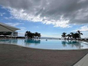 Una amplia piscina al aire libre con palmeras, un edificio de fachada blanca y cielo despejado.