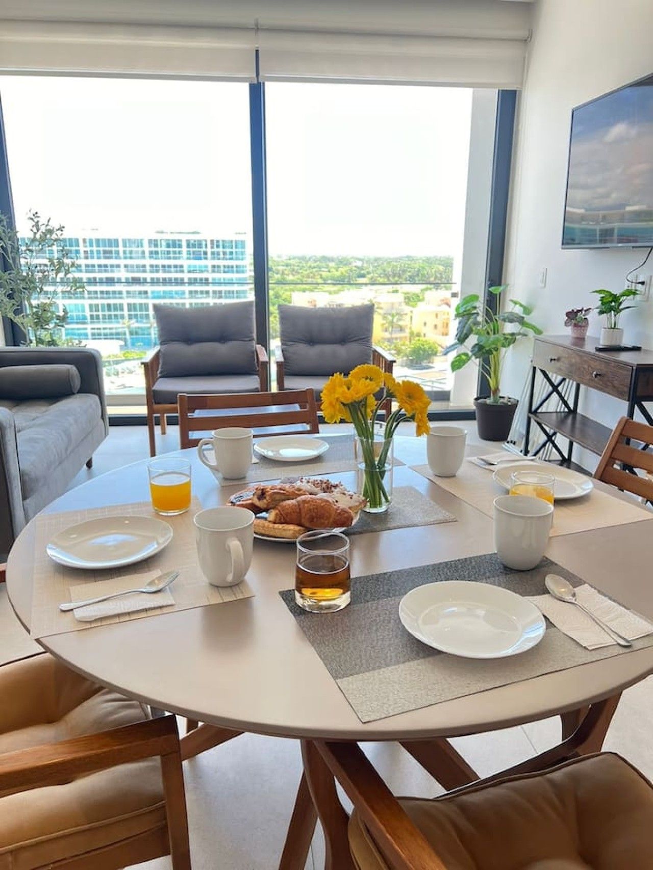 Un coin repas avec une table ronde mise pour le petit-déjeuner, comprenant des assiettes, des tasses et un verre de jus de fruits.