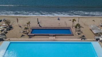 A swimming pool adjacent to a beach with lounge chairs and umbrellas.