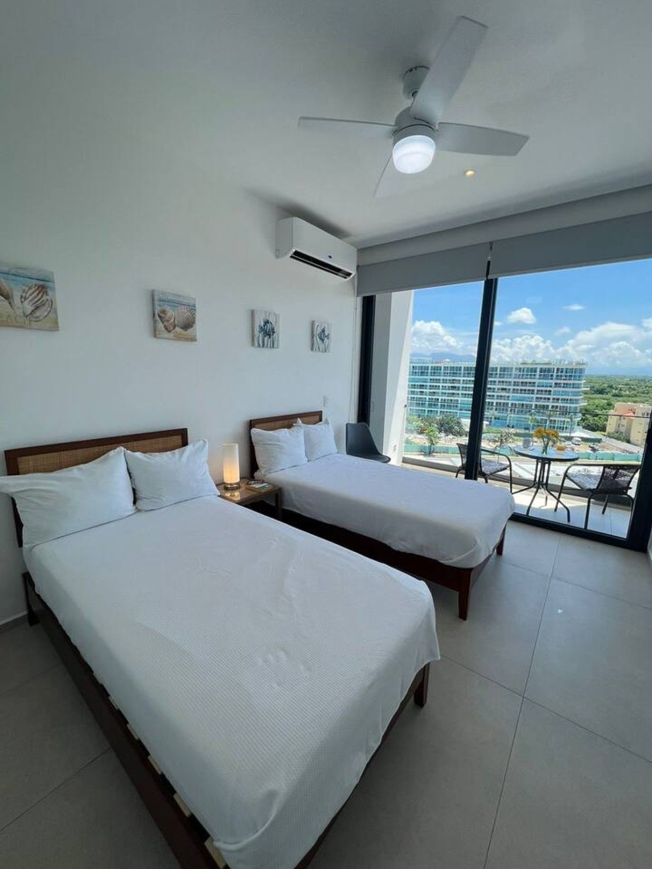 A hotel room with two beds, a ceiling fan, and a balcony with a view of a building.